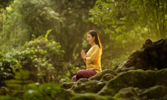 A woman meditates peacefully in a sunlit forest, embodying tranquility and connection with nature.