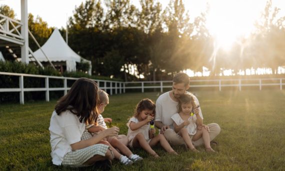 Family sitting on grass enjoying leisure time outdoors, with sun setting in the background.